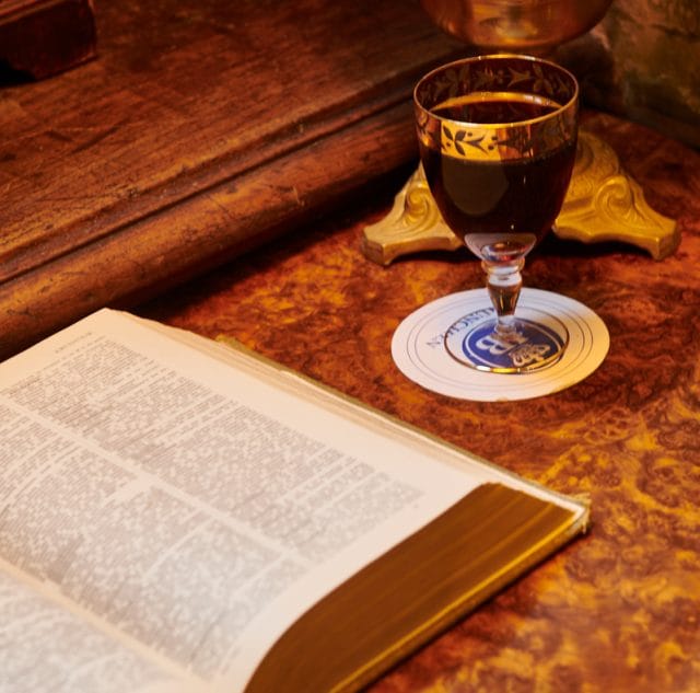 A glass of red wine poured and standing on an antique table inside Kronendal 1713